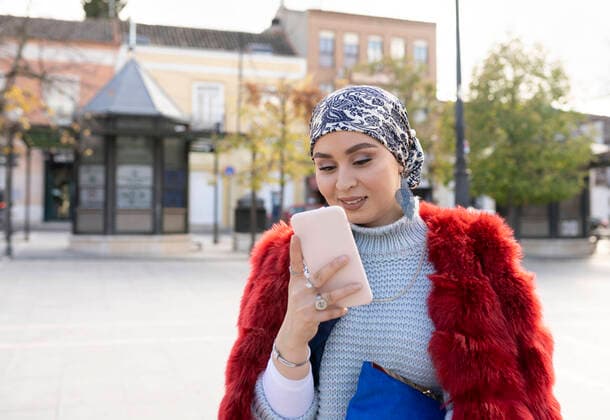 IMAGO Creative: Clickbait, Modetrends Young woman wearing warm clothing using mobile phone while standing in city model released Symbolfoto JCCMF00052