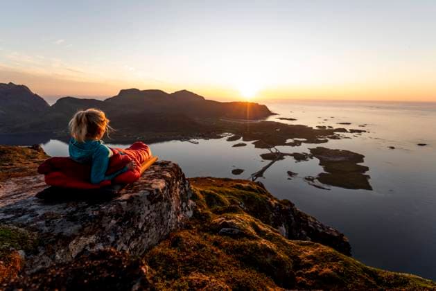 Hiker admiring sunset view while lying in sleeping bag at Volandstinden, Lofoten model released Symbolfoto MALF00248