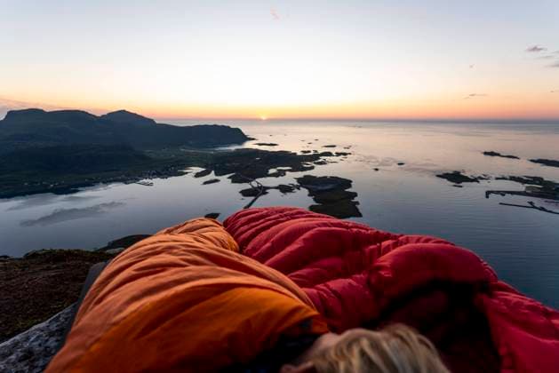 Hiker lying in sleeping bag against sea at Volandstinden, Lofoten, Norway model released Symbolfoto MALF00252