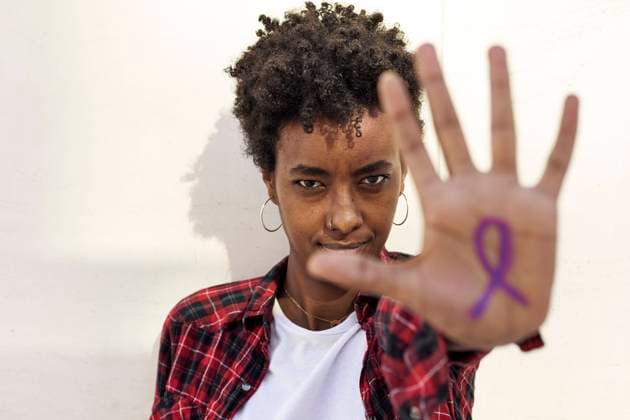 Confident young woman showing purple awareness symbol on palm against white wall during Womens Day model released Symbolfoto VEGF03203