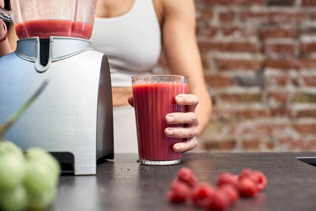 Creative Highlights Symbolfotos Mature woman holding glass of raspberry smoothie by blender on kitchen island model released Symbolfoto property released VEGF03301