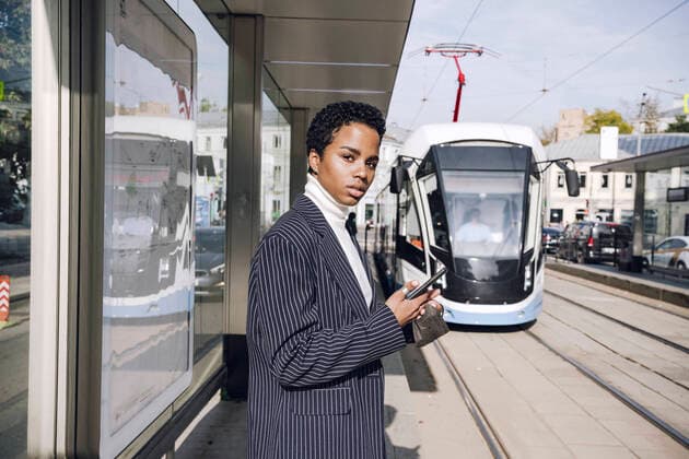 IMAGO Creative: Corporate: Klimaschutz, Digitalisierung und Urbanisierung Young businesswoman with mobile phone waiting for bus at stop on sunny day model released Symbolfoto VYF00294