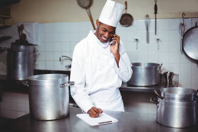 Chef writing on clipboard while talking on phone Chef writing on clipboard while talking on phone in kitchen, model released30s, Mid Adult, Man, Male, Black, Chef, Chefs Whites, Chefs Hat, Uniform, Profession, Professional, Occupation, Job, Worker, Standing, Writing, Clipboard, Pen, Notes, Talking, Conversation, Interacting, Smartphone, Mobile Phone, Cellphone, Phone, Wireless Technology, Communication, Connection, Holding, Kitchen, Kitchen Utensils, Industry, Restaurant, Hotel, Catering, Happy, Expertise, Service, Indoors 