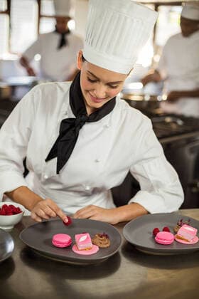 Smiling female chef finishing dessert plates Smiling female chef finishing dessert plates in commercial kitchen, model released30s, Mid Adult, Man, Male, Caucasian, 20s, Young Adult, Woman, Female, Black, Chef, Chefs Whites, Head Chef, Chefs Hat, Uniform, Profession, Professional, Occupation, Job, Worker, Smiling, Cheerful, Finishing, Decorating, Garnish, Garnishing, Dish, Dessert, Sweet, Pastry, Macaroon, Plate, Gourmet, Working, Preparation, Preparing, Food, Kitchen Worktop, Commercial Kitchen, Delicious, Cuisine, Industry, Restaurant, Hotel, Catering, Happy, Expertise, Service, Indoors 