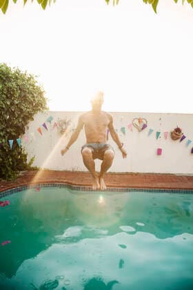 Shirtless man jumping into swimming pool against sky during sunset model released Symbolfoto property released AJOF00299