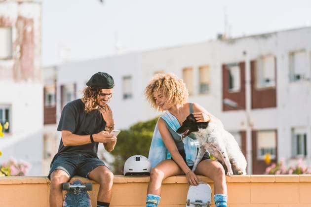Friends using mobile phone while sitting with dog on retaining wall in city model released Symbolfoto DAMF00556