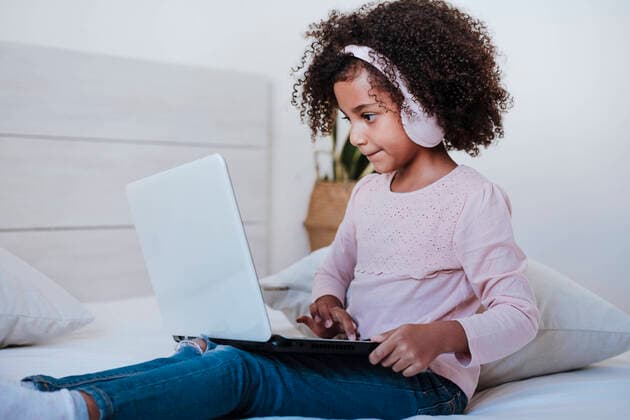 Cute girl using laptop wearing headphone listening music while sitting in bedroom at home model released Symbolfoto property released EBBF00952