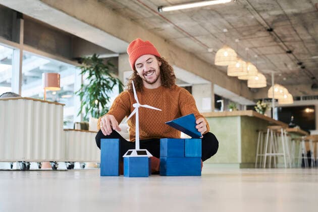 Man playing with toy block and wind turbine while sitting on floor in living room at home model released Symbolfoto property released FMKF06723