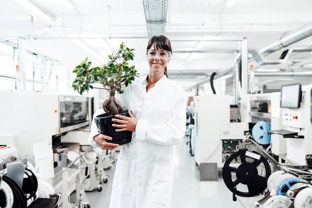 IMAGO Creative: Klimawandel - Zukunft und Innovation Smiling female scientist holding potted plant while standing amidst machineries at laboratory model released Symbolfoto property released JOSEF02177