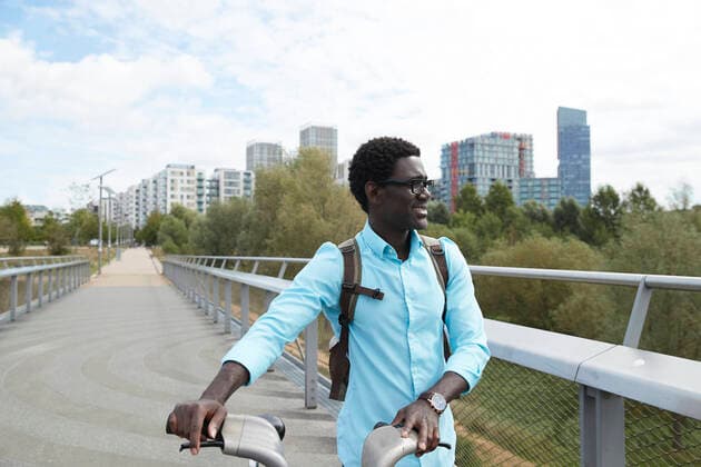 IMAGO Creative: Klimawandel - Zukunft und Innovation Smiling man looking away while walking with bicycle against sky in city model released Symbolfoto PMF01519