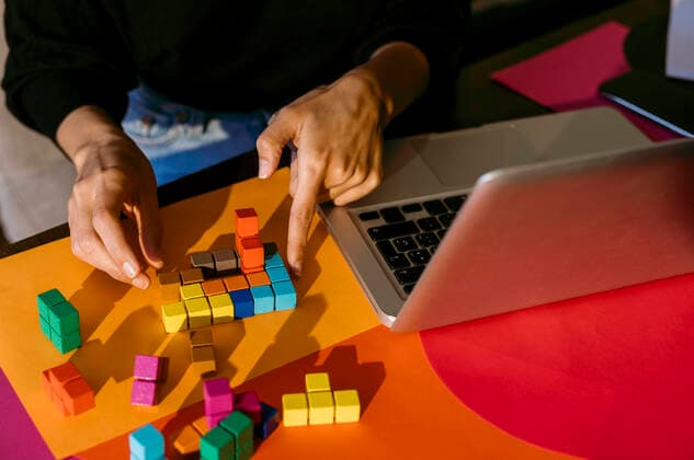 Hands of businesswoman playing with colorful toy blocks by laptop at table model released Symbolfoto property released VABF03803