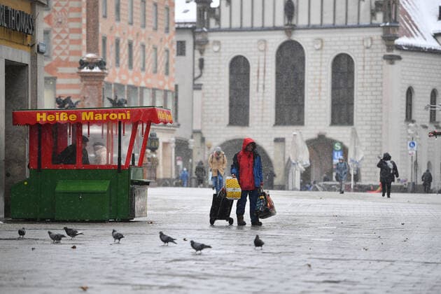 Themenbild Winter in der Coronavirus Pandemie. Verlaengerung Lockdown bis 31.Januar 2021. Leere Strassen und Plaetze.Nur wenige Passanten gehen ueber den Marienplatz in Muenchen am 12.01.2021. Ein Obdachloser geht mit seinem Hab und Gut an einem Heisse Maroni Stand vorbei-im Vordergrund tummeln sich Tauben. Personen,Passanten.