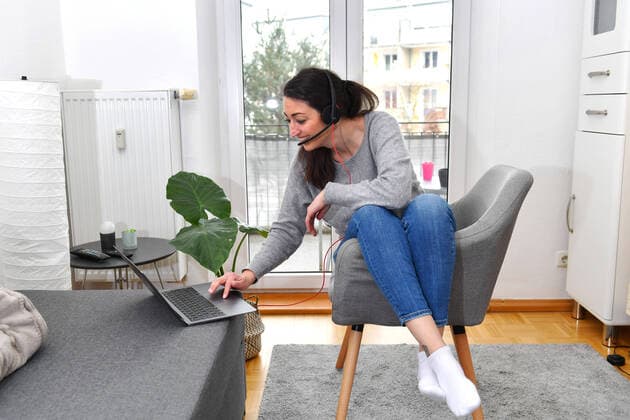 Eine junge Frau sitzt in ihrer Wohnung mit einem Laptop mit Headset und arbeitet im Homeoffice wegen der Corona Pandemie.Teams, MODEL RELEASED!