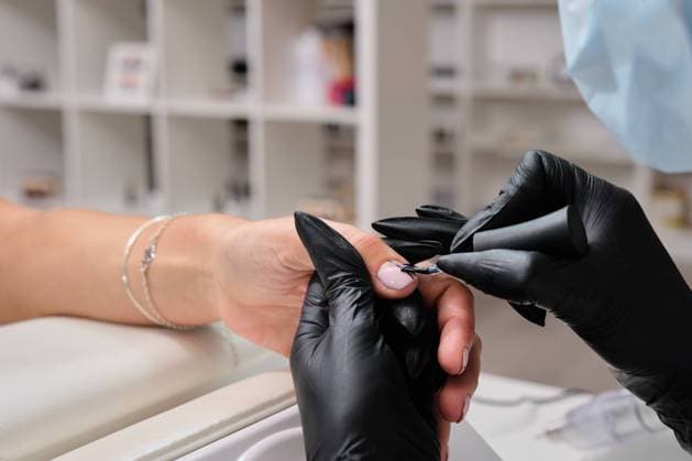 Closeup of crop anonymous master in gloves using metal cuticle pusher while doing manicure for female client in beauty salon, Model released, Property released Copyright: xAntonioxOvejerox MR