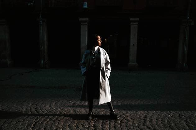 Side view of young ethnic female in coat looking at camera while walking near old stone building in sunny day in city Copyright: xJakexJakabx Model Released