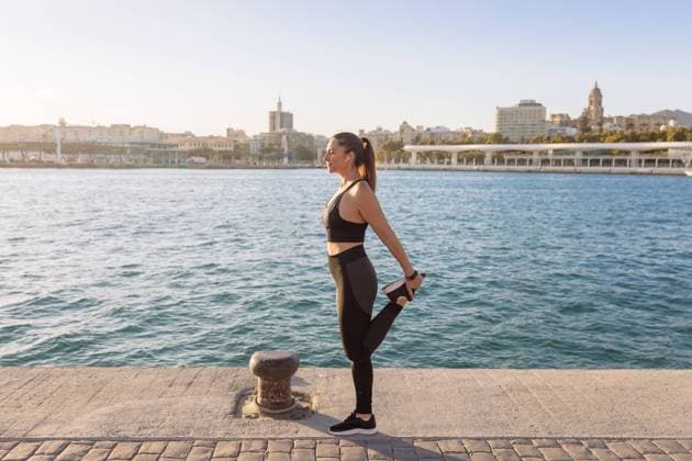 IMAGO Creative: Clickbait, Sport und Fitness Full body side view of fit female in black sportswear stretching legs while exercising on city waterfront during fitness workout Copyright: xMarinaxGallardox Model Released