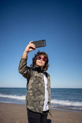 IMAGO Creative, Jahreszeit Herbst, Ferien Boy in sunglasses on the beach taking a self portrait with a mobile on a sunny winter day Copyright: xMikelxPoncex Model Released