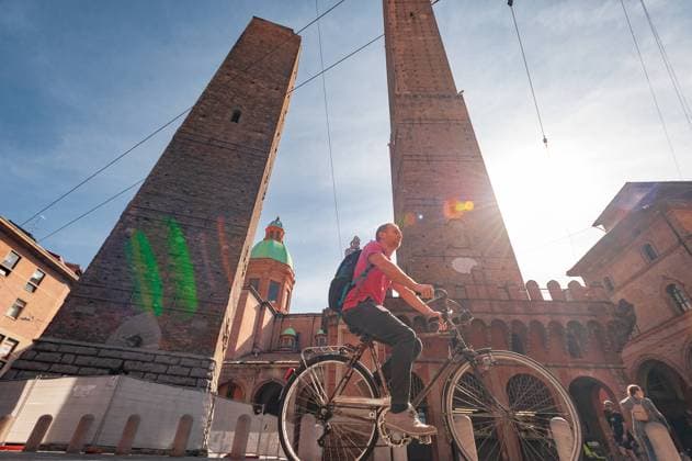 BOLOGNA, ITALY - SEPTEMBER 30, 2019: Tourist on bicykle near Torre Garisenda and Torre Degli Asinelli leaning towers Due Torri. Two towers. Statue des Hl. Petronius Copyright: xVitaliixKliuiev(Vitleo)x
