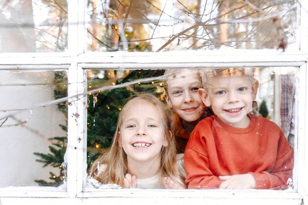 Smiling siblings looking through window from home model released Symbolfoto property released EYAF01446