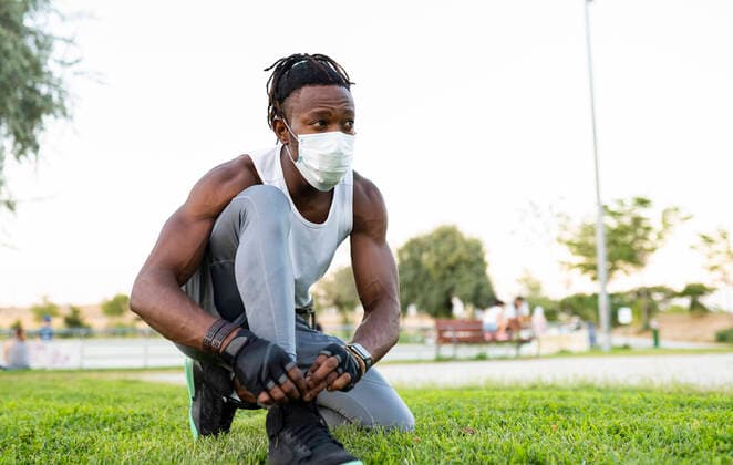 IMAGO Creative: Kulturelle Folgen der Pandemie: Gesundheitsbewußtsein und Alleinsein Athlete wearing face mask tying lace of shoe while crouching on ground model released Symbolfoto JCCMF00165