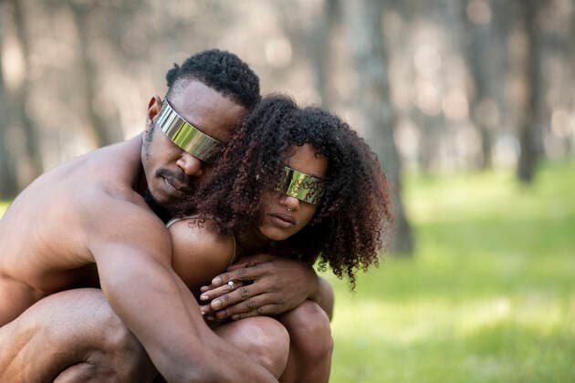 Two professional dancers wearing futuristic goggles crouching and embracing in middle of forest model released Symbolfoto JCCMF00599