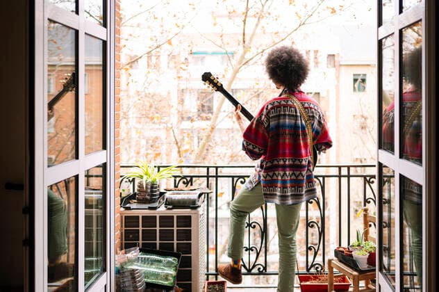 IMAGO Creative: Lokalhelden - Kunst und Kultur Afro young man practicing guitar in balcony seen through doorway model released Symbolfoto property released JCMF01803