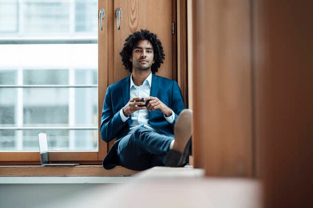 IMAGO Creative: Kreative Renaissance -- der junge Entrepreneur Confident male entrepreneur holding coffee cup while sitting against window at office model released Symbolfoto property released JOSEF02933