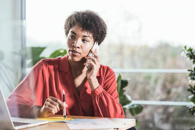 Woman talking on mobile phone and looking at laptop at desk model released Symbolfoto property released UUF22462