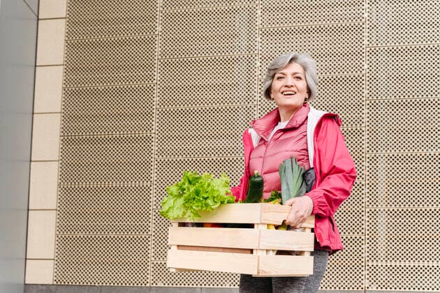 Happy mature woman with food crate against iron pattern wall model released Symbolfoto VYF00371