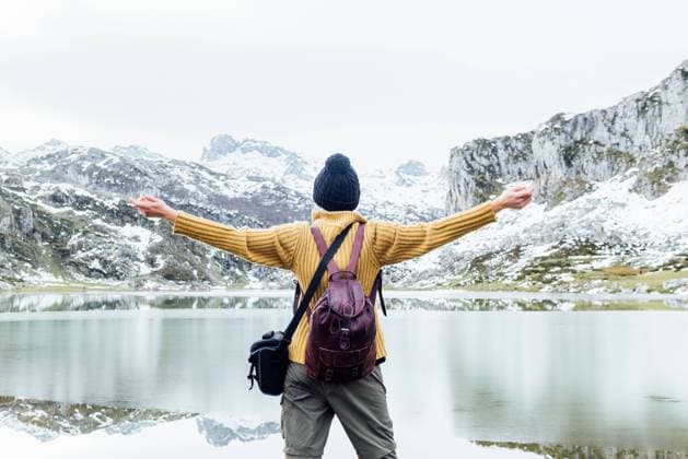 IMAGO Creative: Wintersport, Mode Back view anonymous female traveler standing with arms outstretched on cold lakeside and admiring severe rocky mountains covered with snow on winter day, Model released Copyright: xAlbertoxMenendezx MR