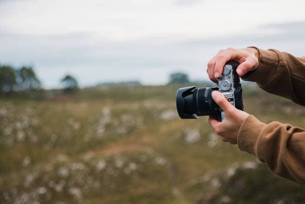 IMAGO Creative: Kreative Renaissance -- der junge Entrepreneur Crop anonymous male photographer in warm jacket taking pictures on professional camera of vast grassy field on overcast day Copyright: xErikaxAnesx Model Released