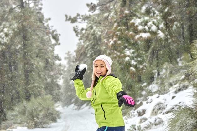 IMAGO Creative: Alternativer Wintersport Excited girl in warm clothes and hat throwing snowball while having fun in frozen winter woodland and looking away with happy smile, Model released Copyright: xGabrielxTrujillox MR