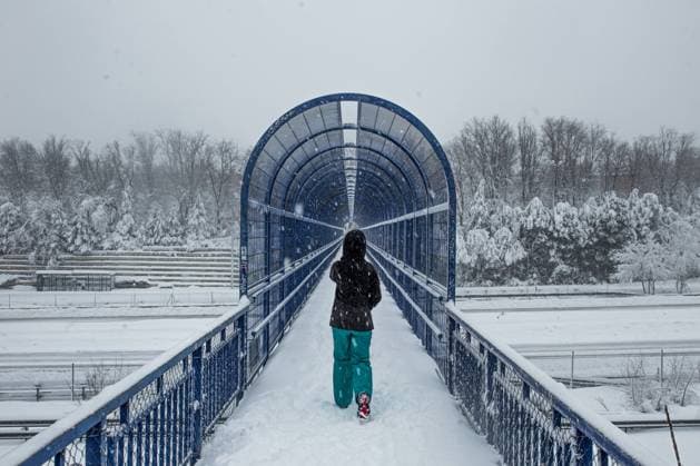 Back view full body female in warm clothes strolling on snowy pedestrian bridge over road on cold winter day during heavy snowfall Copyright: xIsraelxDexLagox Model Released