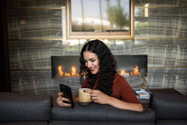 Creative Highlights Symbolbilder Happy young woman holding phone and drinking coffee on couch Portland, OR, United States CR_CHBR210127-130626-01 ,model released, Symbolfoto