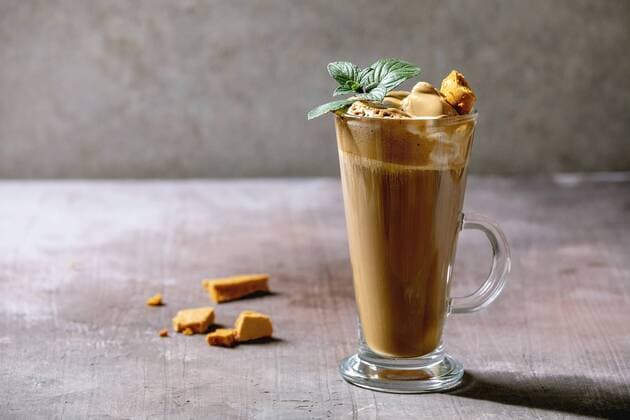 Dalgona frothy coffee trend korean drink latte espresso with coffee foam in tall glass, decorated by dalgona cinder toffee candy and mint. Grey concrete background. ÂNatashaBreen REDA&CO 1028_29_NBR8918
