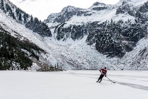 IMAGO Creative: Alternativer Wintersport Man playing hockey near snowy mountains on frozen lake in Canada Canada, British Columbia, Pemberton CR_PSFZ210201-623643-01 ,model released, Symbolfoto