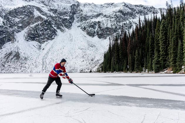 IMAGO Creative, Jahreszeit Winter, Eislaufen Young man playing ice hockey on lake near snow covered mountain Canada, British Columbia, Pemberton CR_PSFZ210201-623652-01 ,model released, Symbolfoto