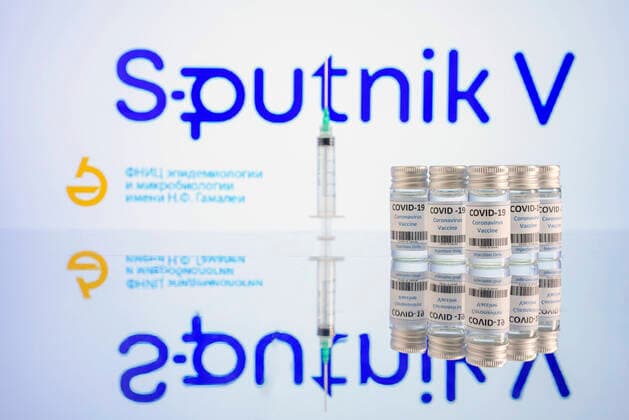 Impfdosen und Impfspritzen stehen auf einem Tisch vor dem Logo des Impfstoffs Sputnik V des russischen Gamaleja-Institut für Epidemiologie und Mikrobiologie. (Themenbild, Symbolbild)