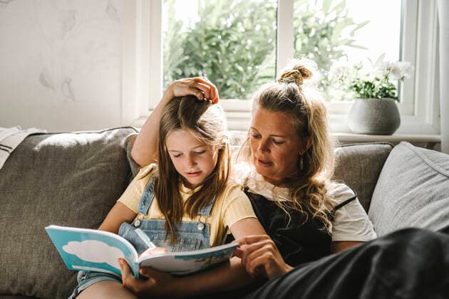 Daughter writing in book while sitting by mother on sofa at home Sweden, Gothenburg, model released, property released Copyright: xMaskotx , MA83753