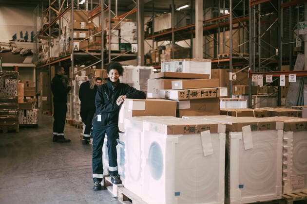 Smiling female entrepreneur leaning on box containers at distribution warehouse Sweden, Stockholm, model released, property released Copyright: xMaskotx , MA84139