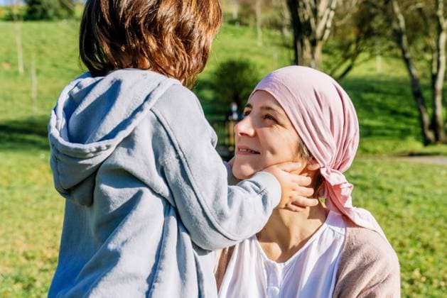 IMAGO Creative: Brustkrebsmonat Unrecognizable daughter drawing smile with fingers on mother s face with cancer wearing pink head scarf standing on green park looking at each other Copyright: xLuisxManuelxMunozx Model Released