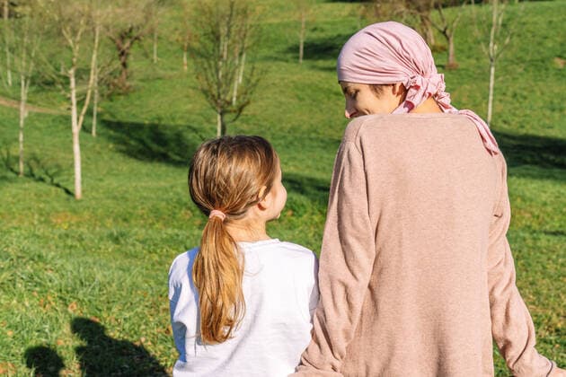IMAGO Creative: Brustkrebsmonat Back view of tender calm mother with cancer wearing pink head scarf speaking with little daughter sitting on a bench on green park Copyright: xLuisxManuelxMunozx Model Released