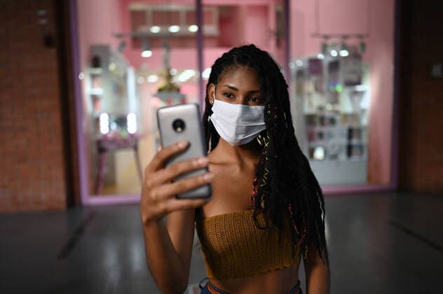 Creative Highlights Symbolbilder Portrait of attractive young afro latin woman wearing a facemask and doing a videocall on smartphone in a commercial mall, Colombia, Model released Copyright: xNanoxCalvox MR