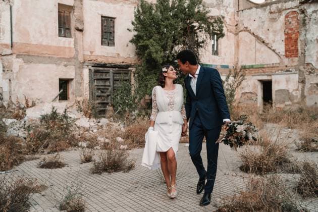Young glad multiracial groom and bride looking at each other while strolling on walkway against aged construction on wedding day Copyright: xVictorxGonzalezx Model Released