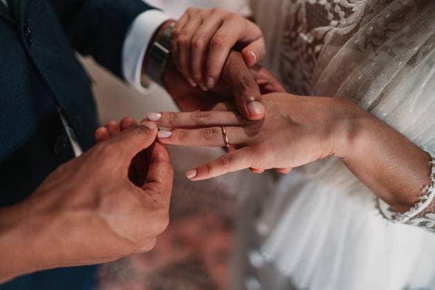 High angle side view of cropped unrecognizable ethnic groom putting ring on finger of bride in fancy wedding gowns holding hands gently with affection Copyright: xVictorxGonzalezx Model Released
