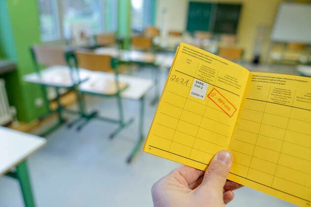 Symbolbild Schule und Klassenzimmer im Lockdown Symbolfoto eines Impfpass mit Impfstempel gegen das Coronavirus mit Klassenzimmer einer Schule im Hintergrund. Wann werden Lehrer und Schueler geimpft. Deutschland