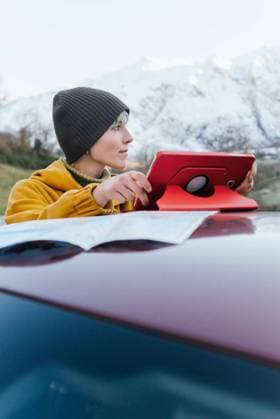 IMAGO Creative: Klimawandel - Nachhaltiges Reisen Content young female in warm clothes browsing tablet on car roof and looking away while standing on mountainous terrain on freezing winter day, Model released Copyright: xAlbertoxMenendezx MR