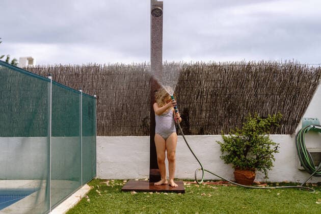 Cute little girl in swimsuit walking and watering green lawn from hose during summer holidays in countryside Copyright: xAngelxSantamariax Model Released
