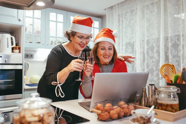 Sincere homosexual mature women in Santa hats with champagne watching netbook with video chat during New Year holiday in kitchen Copyright: xDanixNavarrox Model Released