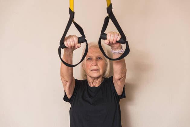 Elderly female athlete in sportswear with gray hair working out with straps while looking at camera in gym Copyright: xErikaxAnesx Model Released